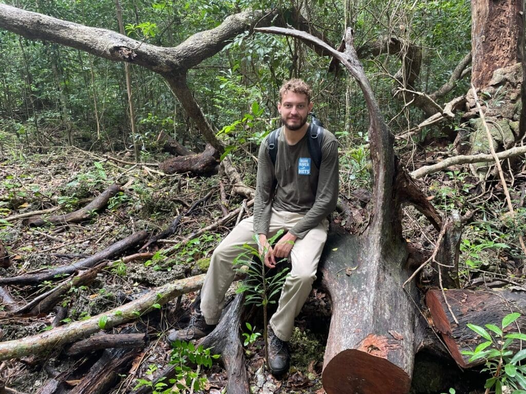 Expedition team member in a Blue River Diets top sitting on a fallen tree in the forest